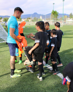 grupo de niños uniformados de negro en un campo de futbol escuchando a su entrenador