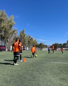 Grupo de niños en un campo de fútbol, vestidos con camisetas negras y detalles naranjas, practicando futbol